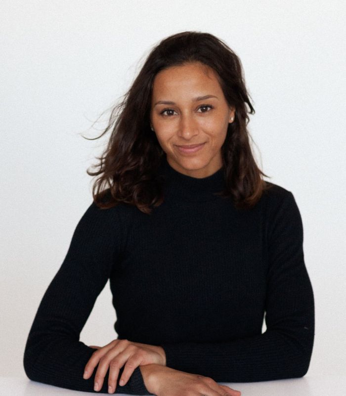 Portrait d'Anne Perrin, souriante, accoudée à une table blanche